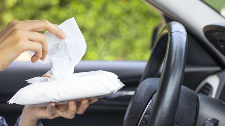 Woman's hand disinfecting the steering wheel of her car with baby wipes